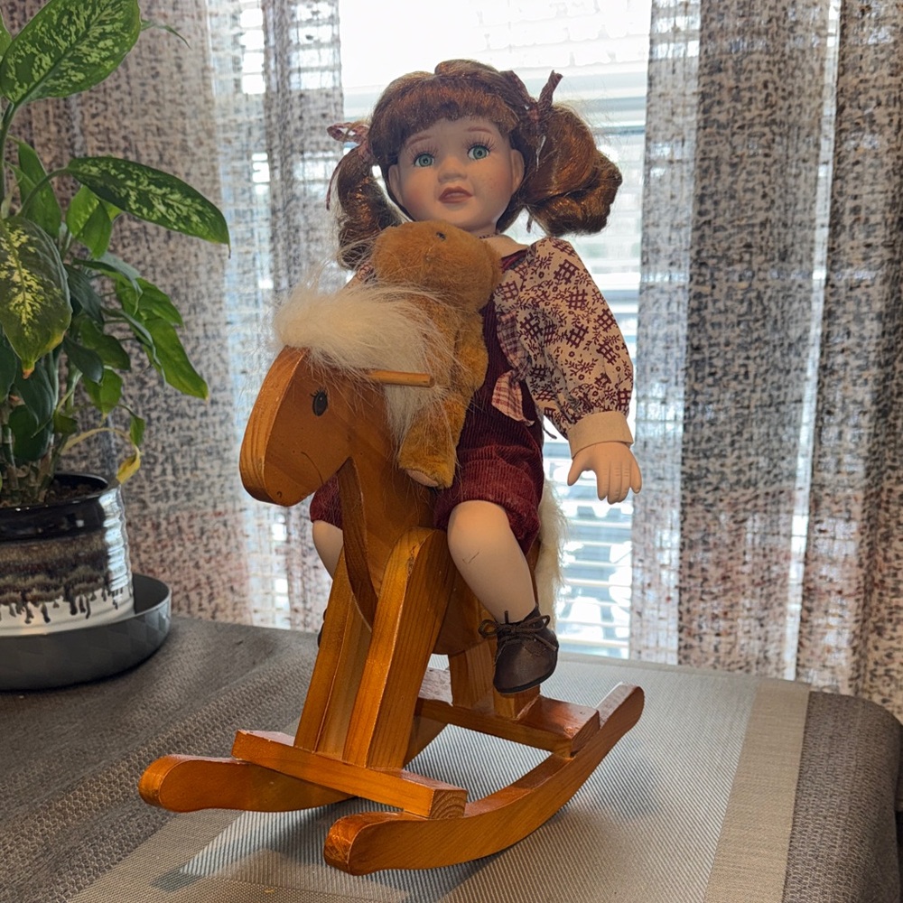 Vintage porcelain doll on a wooden rocking horse with a teddy bear.
